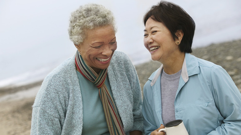 Two older women laughing together on a hillside wearing a gray jumper and a blue blouse