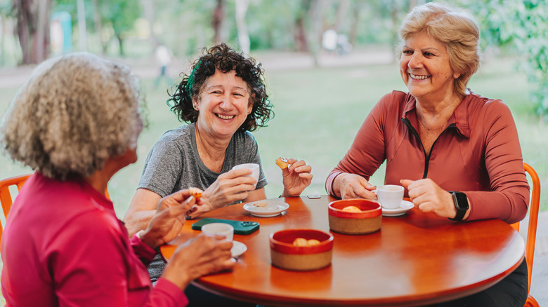 Three older women sharing a snack and espresso around a table