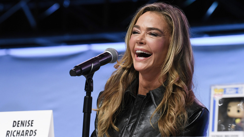 Denise Richards laughing in front of a microphone and next to a Funko pop