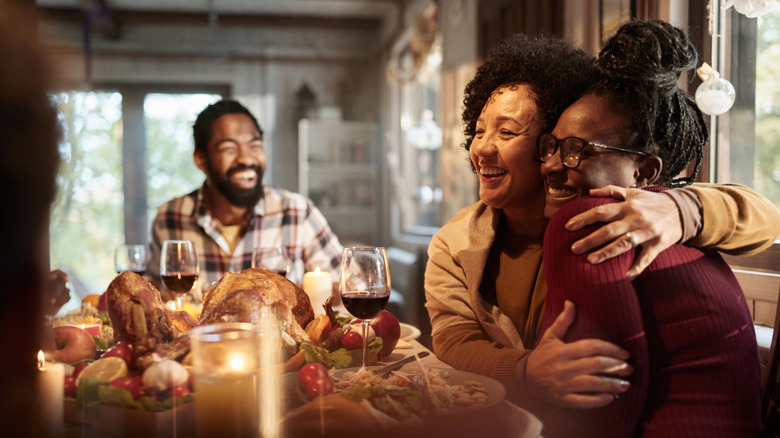 Friends hug and laugh around a full Thanksgiving dinner table