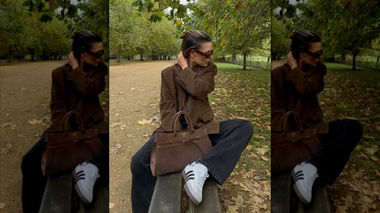A woman sitting on a park bench wearing dark pants and a suede blazer