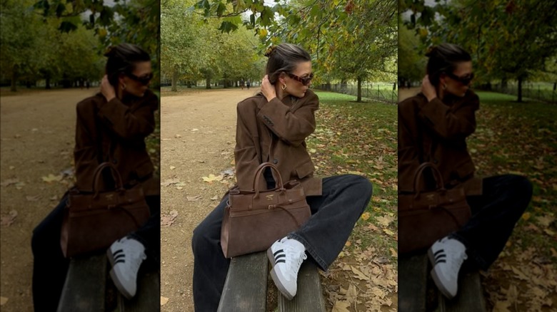 A woman sitting on a park bench wearing dark pants and a suede blazer