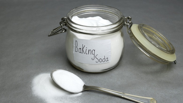 A jar of baking soda next to a spoon spilling over with baking soda