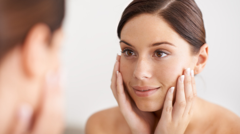 woman looking in mirror hands on face