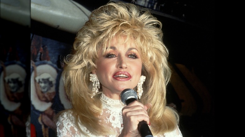 Dolly Parton speaking into a microphone with high volume hair around 1990