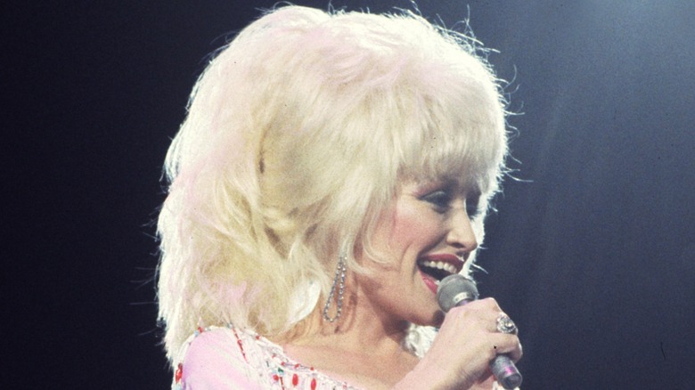 Dolly Parton smiling on stage while wearing a huge blond wig