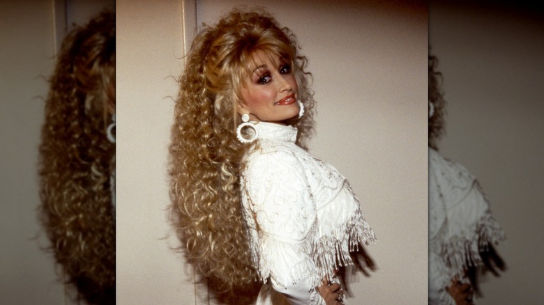 Dolly Parton looking over her shoulder while wearing a super long, curly wig and a fringe outfit