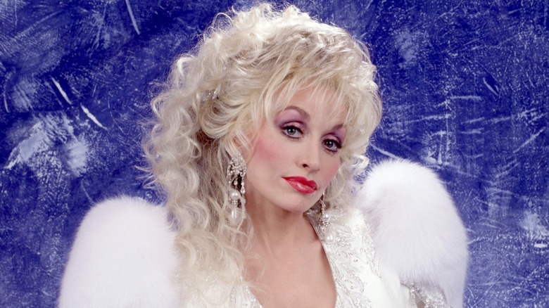 Dolly Parton posing in a white outfit in front of a blue background