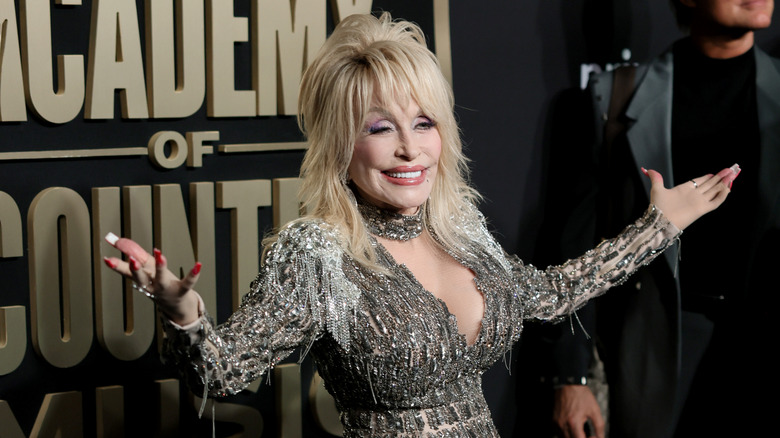 Dolly Parton holding her arms out wide on the red carpet