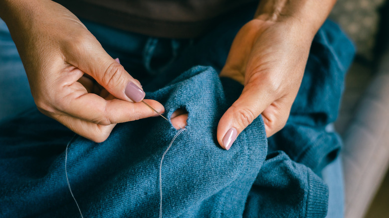 Hands repairing a hole in a sweater