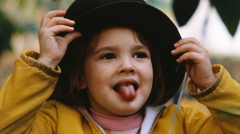 Drew Barrymore wearing a coat and hat while sticking her tongue out in 1979