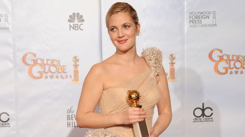 Drew Barrymore posing with a Golden Globe Award in a champagne dress in 2010