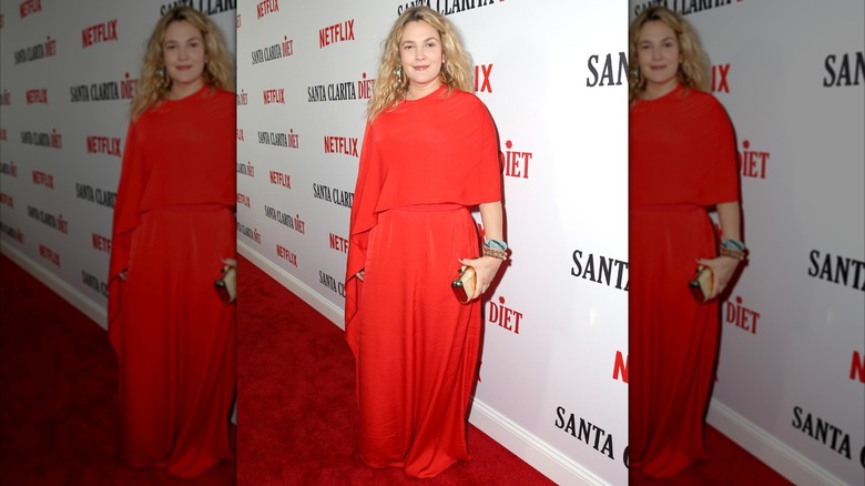 Drew Barrymore smiling in an oversized red jumpsuit on the red carpet in 2016