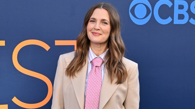 Drew Barrymore smiling on the red carpet in 2025 in a beige suit and pink tie.
