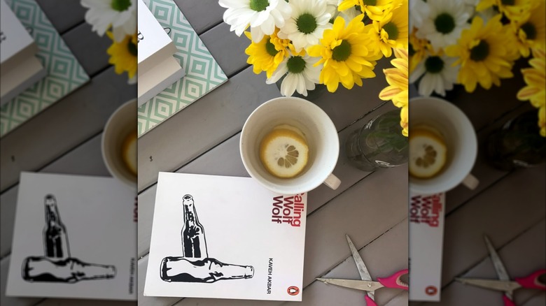 A copy of "A Wolf Calling a Wolf" laying next to scissors and a cup of tea on a table