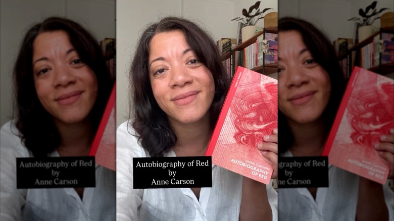 A woman holding up a copy of "The Autobiography of Red" next to her face