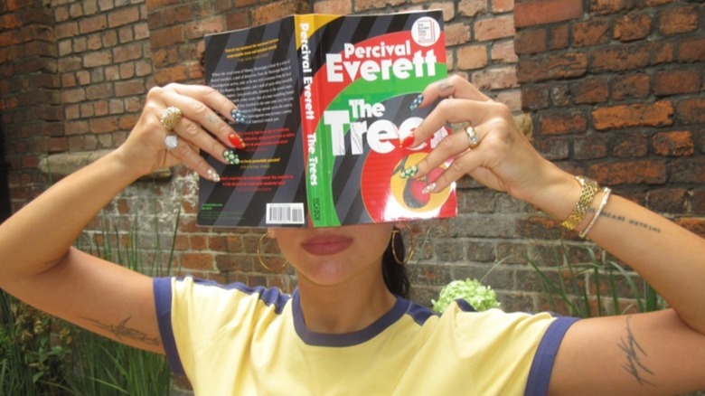 Dua Lipa covering her eyes with  The Trees by Percival Everett