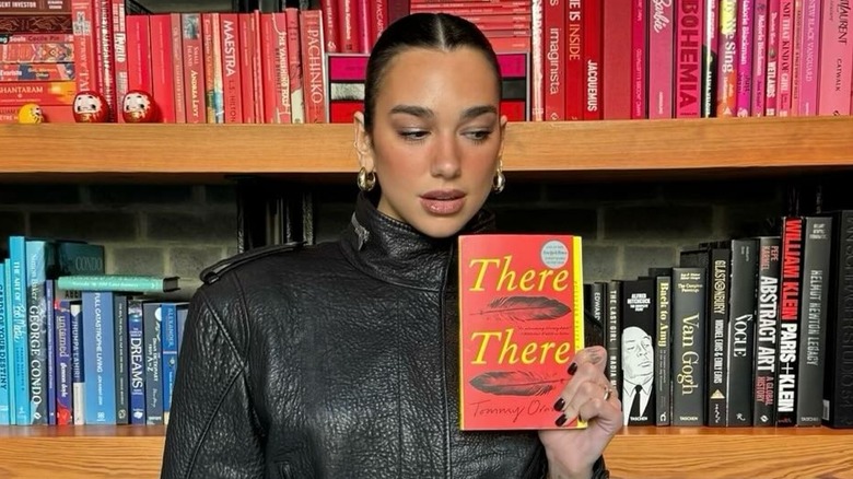 Dua Lip holding a copy of There There by Tommy Orange