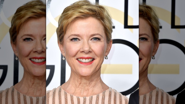Annette Bening wearing beige dress and coral lipstick with drop earrings