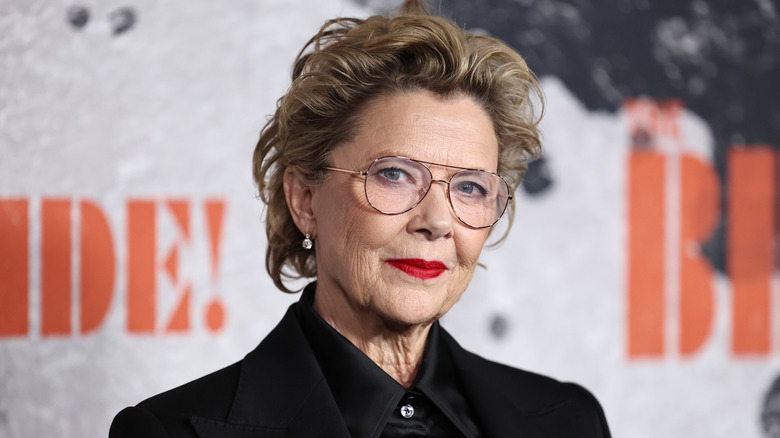 Annette Bening wearing a black blazer and red lipstick with aviator glasses