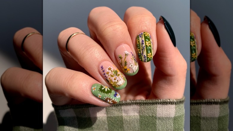 Folding hand showing nails with a variety of green, yellow, and brown-colored designs