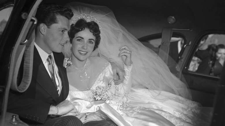 Elizabeth Taylor smiling at the camera while in a car with groom Conrad Nicholson Hilton Jr.