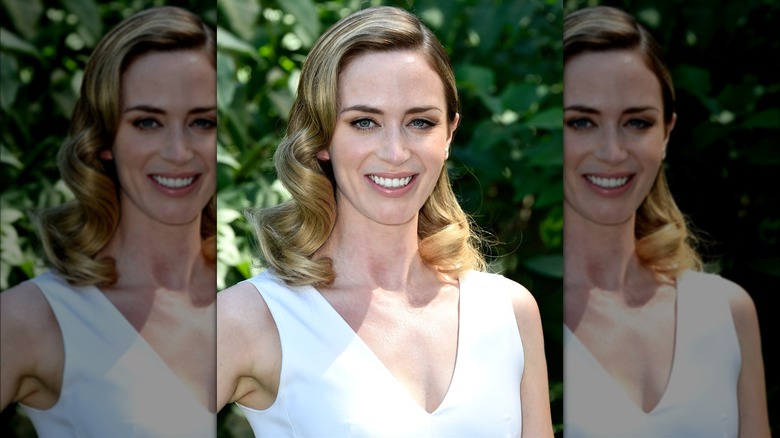 Emily Blunt smiling with curled hair while wearing a white top in 2016