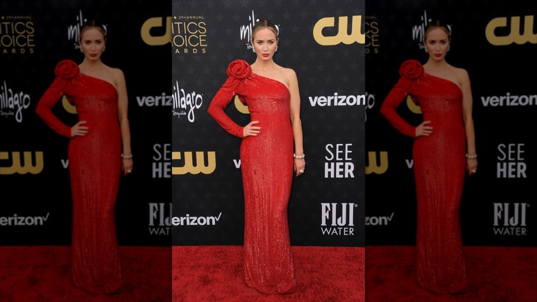 Emily Blunt poses in red lipstick and a red sequin dress with one sleeve.