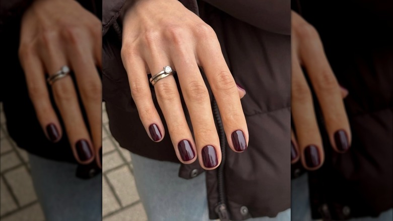 A hand with an engagement ring and burgundy nails