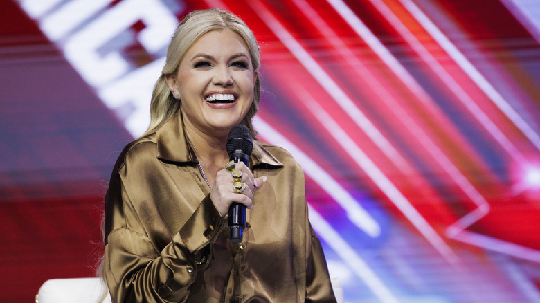Erika Kirk on stage in a brown shirt holding a microphone