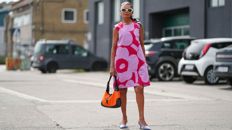 A woman in a pink and red pattern shift dress with sunglasses and a head scarf