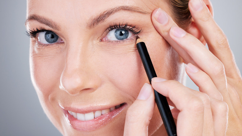 A closeup of a smiling woman applying eyeliner