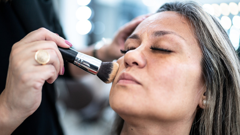 A woman having foundation applied to her skin with a brush