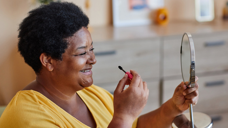 Close-up of mature, brunette woman holding a mascara wand near her brown eye