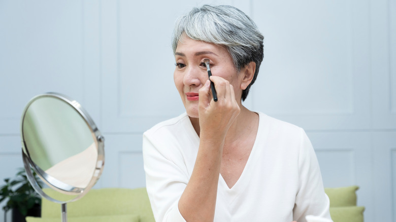 Senior woman putting on eye makeup