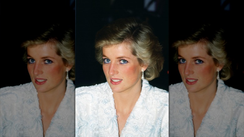 Princess Diana smiles wearing a white blazer and blue eyeliner