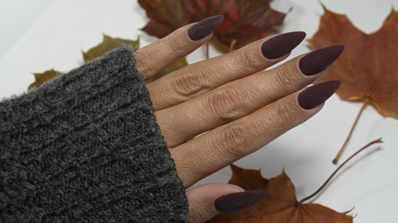 A woman holding out nails in front of fall leaves