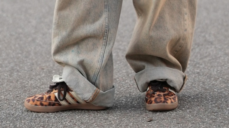 A woman's feet wearing leopard print sneakers with turned up jeans