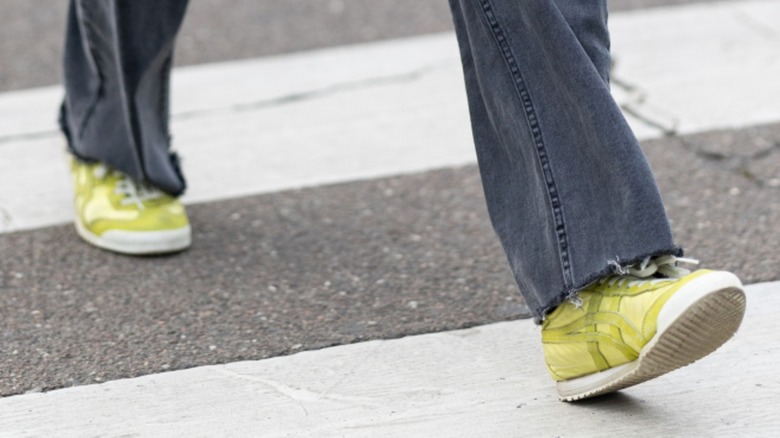 A woman's feet walking in yellow sneakers while wearing dark jeans