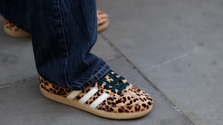 A person's feet wearing leopard print sneakers with dark jeans