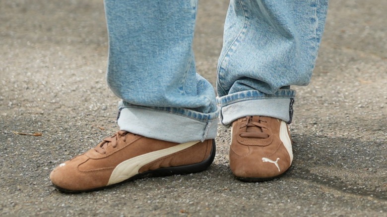 A woman's feet wearing brown, slim sneakers with turned up blue jeans