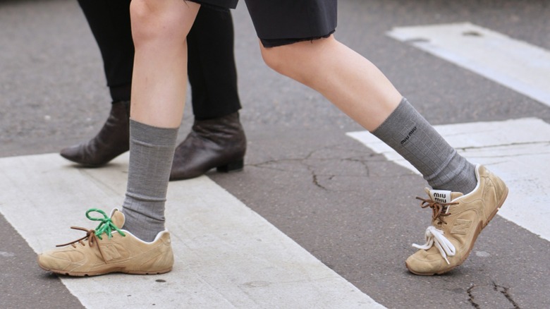 A woman's feet crossing the street while wearing tan suede sneakers
