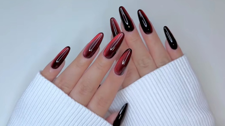 A woman showing a velvet merlot manicure with white sweater sleeves
