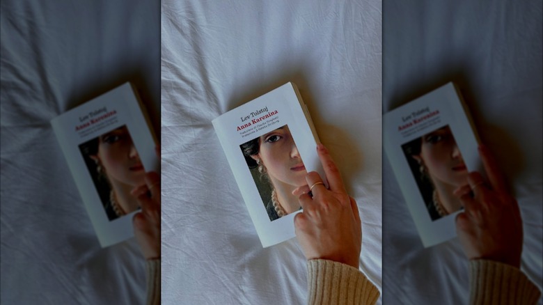 A copy of "Anna Karenina" on a white sheet with a hand touching it