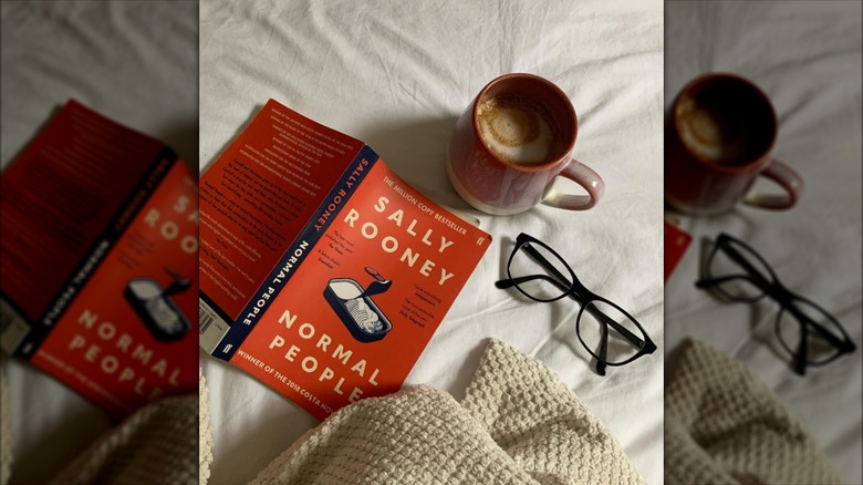 A copy of "Normal People" laying on a white sheet next to reading glasses and a cup of coffee