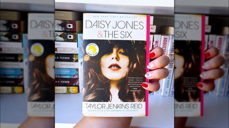 A hand holding a paperback copy of "Daisy Jones & the Six"