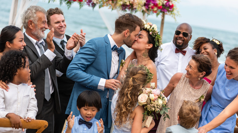 A family gathered around a kissing bride and groom with the ocean in the background