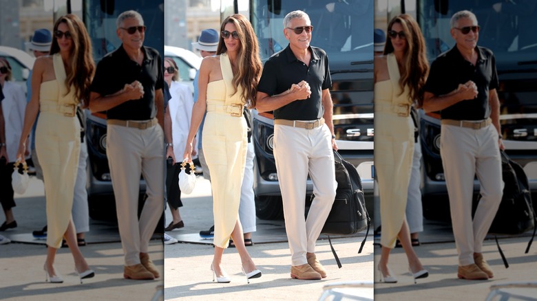 Amal Clooney wearing a yellow dress and George Clooney wearing a black polo shirt and cream trousers