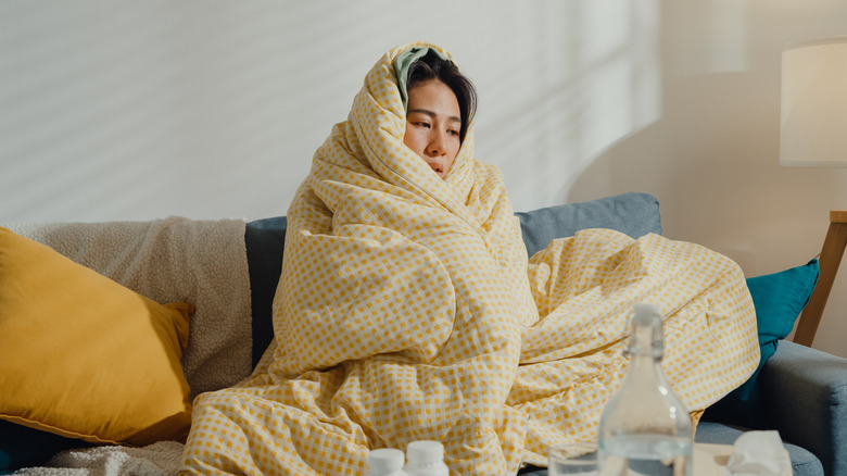 Woman looking sick while wrapped in a blanket on the couch