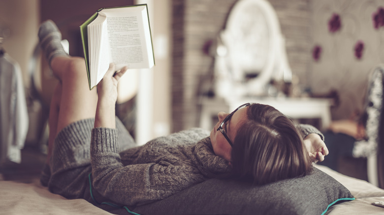 Woman with glasses laying down reading a book